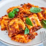 ravioli and meat sauce on white plate with fork